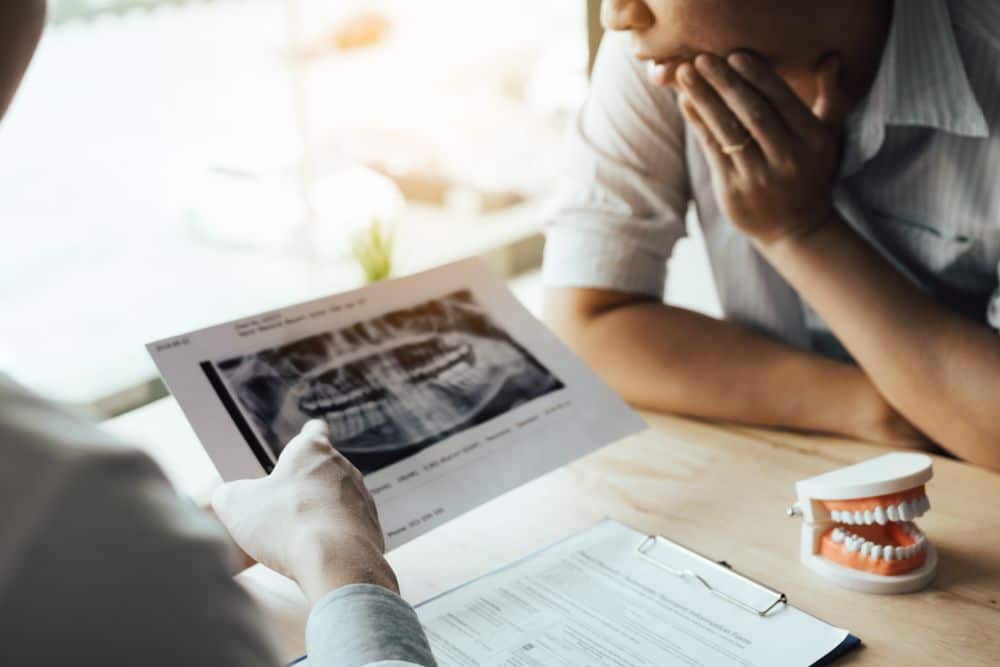 two people sitting down at a table looking and point at x-ray of teeth
