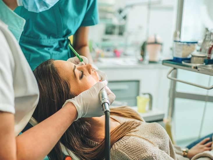 two dentists working on a woman's mouth with tools as she lays in dental chair